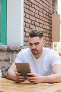 Genç adam bir tablet kullanarak kafe Cafe. Açık havada