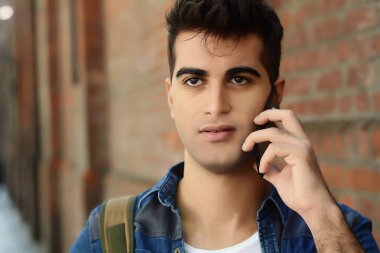 Duvara karşı telefonda konuşan genç latin adam portresi. Açık havada.