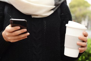 Kağıt bardak kahve içme ve bir onu kullanarak güzel kadın kış sokakta telefon. Concep götür