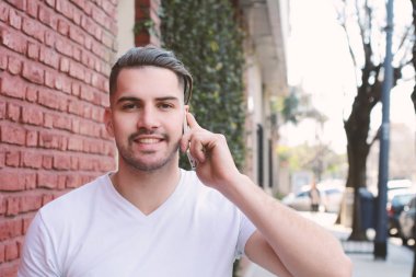 Duvara karşı telefonda konuşan genç adam portresi. Açık havada.