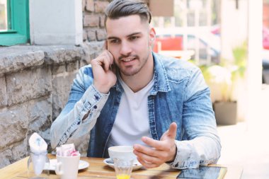 Genç adam telefonda konuşurken kafede. Açık havada