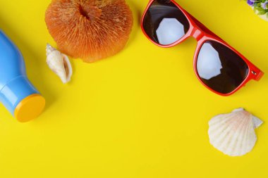 Sarı zemin üzerine üstten görünüm güneş gözlüğü, kabukları, deniz yıldızı ve güneş kremi. Yaz konsepti.