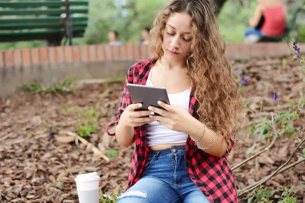 Genç öğrenci kız ile bir tablet ve sonbaharda park üzerinde oturan bir tek kullanımlık kahve fincanı.