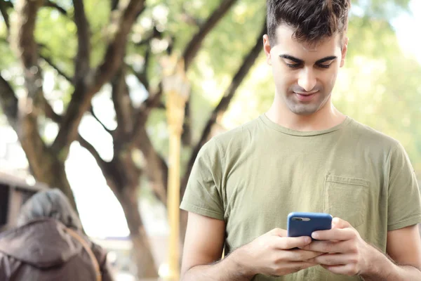 Telefonunda daktilo eden genç Latin adamın portresi. Açık havada..