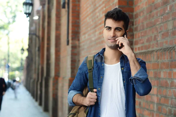 Duvara karşı telefonda konuşan genç latin adam portresi. Açık havada.