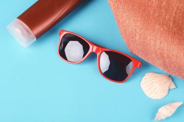 Üstten Görünüm güneş gözlüğü, kabukları, deniz yıldızı ve güneş kremi ile boşaltmak. Yaz konsepti. Açık mavi renkli 