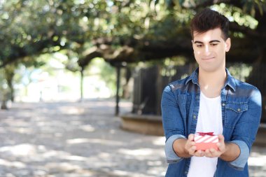 Bir kırmızı hediye kutusu ile genç bir Arap adam portresi. Açık havada