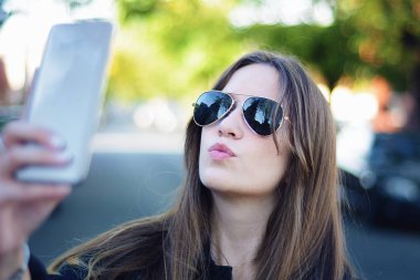 Selfie onun smartphone ile alarak güzel genç bir kadın portresi. Açık havada.