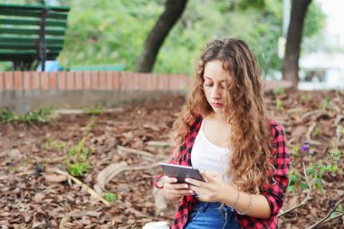 Genç öğrenci kız ile bir tablet ve sonbaharda park üzerinde oturan bir tek kullanımlık kahve fincanı.