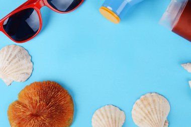 Üstten Görünüm güneş gözlüğü, kabukları, deniz yıldızı ve güneş kremi ile boşaltmak. Yaz konsepti. Açık mavi renkli 