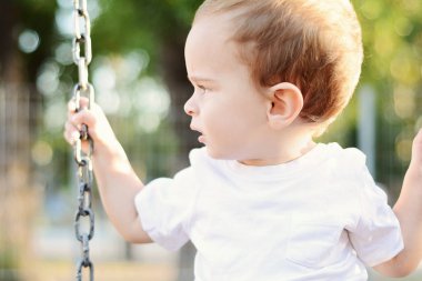 Şirin bebek çocuk bir parkta bir salıncak üzerinde eğleniyor.