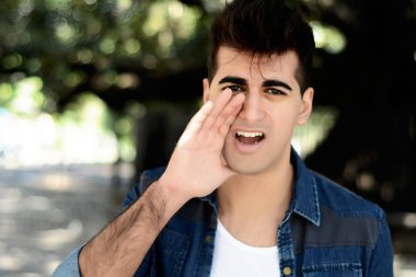 Genç latin adam kameraya bağırarak portresi. Açık havada