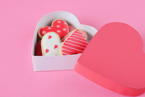 Heart shaped cookies decorated for Valentine's Day in red heart shaped box on pink background