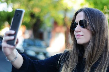 Selfie onun smartphone ile alarak güzel genç bir kadın portresi. Açık havada.