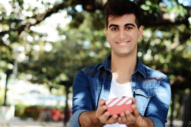 Bir kırmızı hediye kutusu ile genç bir Arap adam portresi. Açık havada