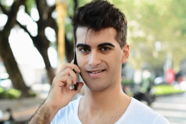 Sokakta telefonda konuşan genç latin adam portresi. Açık havada.
