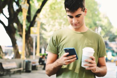 Holding kahve ve okuma iletisi yaptığı telefon genç adam. Açık havada.