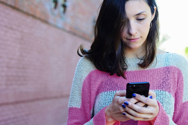 Beautiful young woman sending message with smartphone on the street.