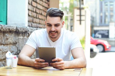 Genç adam bir tablet kullanarak kafe Cafe. Açık havada