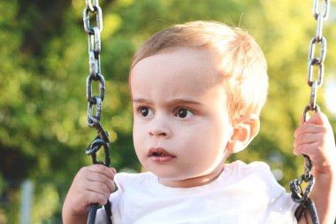 Şirin bebek çocuk bir parkta bir salıncak üzerinde eğleniyor.