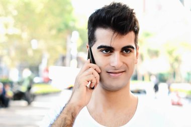 Sokakta telefonda konuşan genç latin adam portresi. Açık havada.
