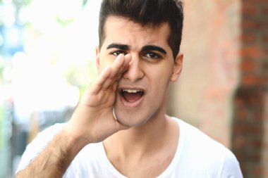 Genç latin adam kameraya bağırarak portresi. Açık havada