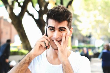 Endişeli genç adam bir parkta telefonda konuşuyor. Açık havada. Teknoloji kavramı.