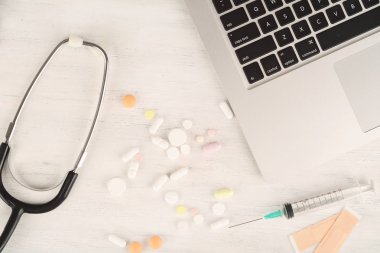 Üstten Görünüm dizüstü bilgisayar, not defteri, stetoskop, ilaç şişeleri ve şırınga doktorun masasından. Modern tıp işyeri 