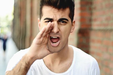 Genç latin adam kameraya bağırarak portresi. Açık havada