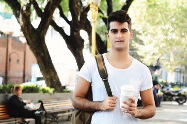 Kahve güneşli parkta tutan genç çekici bir adam. Take away kavramı