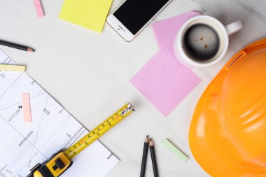 Planlara yakın çekim, mezura, bir fincan kahve ve sarı miğfer. Mühendis kavramı