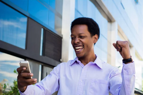 Successful professional young businessman excited with smartphone outside office building. Businessman enjoys success in job.