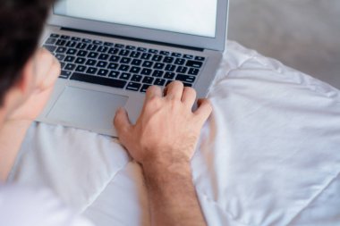 Mutlu genç adam yatağının üzerinde beyaz ekranlı dizüstü bilgisayar kullanarak. Kapalı