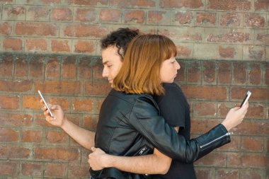 Her biri kendi akıllı telefonuna bakarken genç çift sarılıyor.