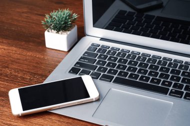 Ahşap masada siyah ekranlı dizüstü bilgisayar ve telefon.