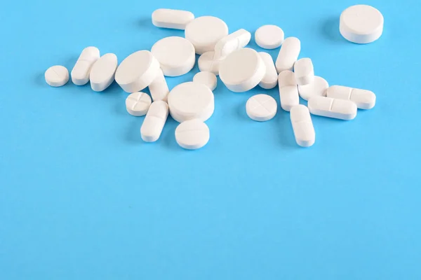 Pile of white pills on light blue background — Stock Photo, Image