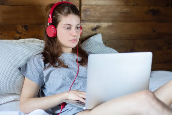 Młoda kobieta za pomocą laptopa i słuchawki w łóżku. — Zdjęcie stockowe