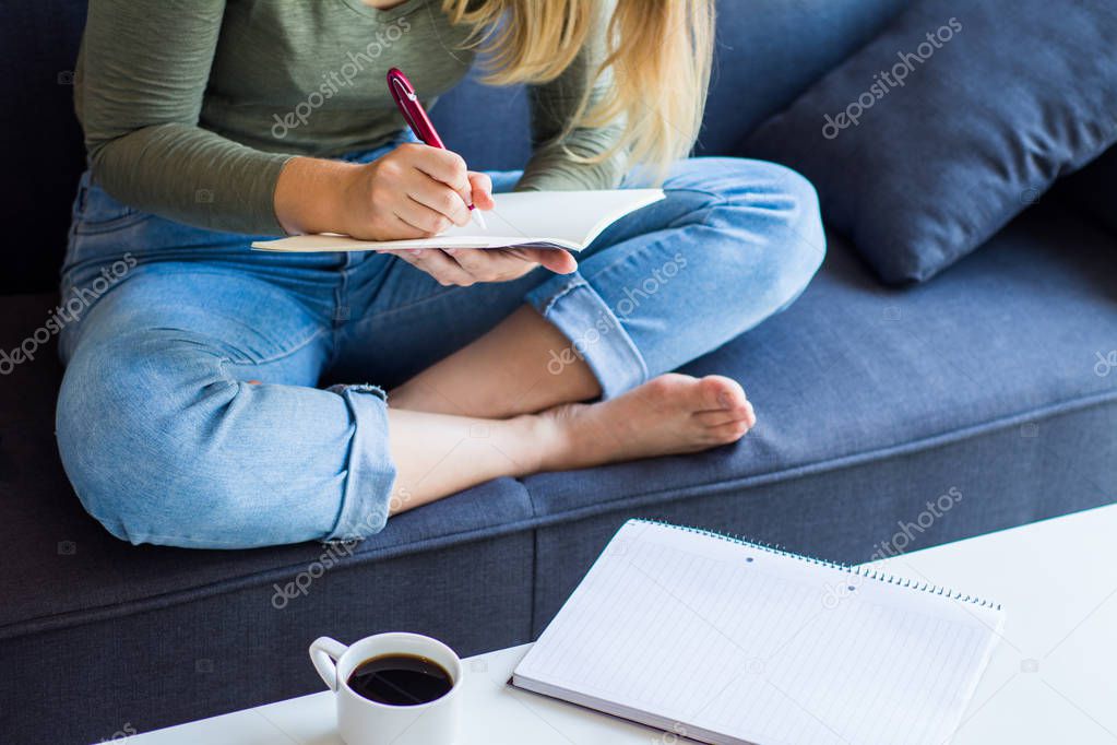 Woman writing on couch at home