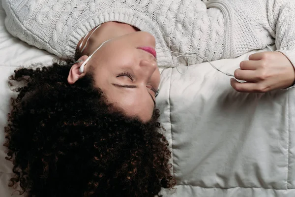 Young woman enjoying music on bed.