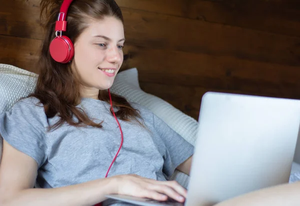 Młoda kobieta za pomocą laptopa i słuchawki w łóżku. — Zdjęcie stockowe