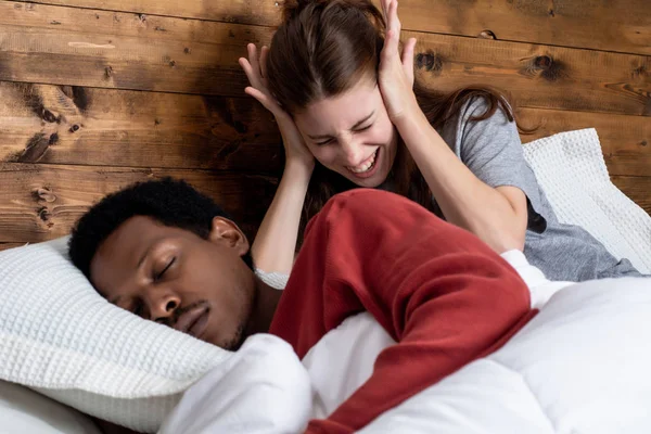 Mulher bloqueando ouvidos com as mãos enquanto o homem ronca na cama — Fotografia de Stock