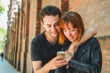 Sokakta eğlenen ve cep telefonu kullanan genç bir çiftin portresi. İlişki ve teknoloji kavramı.