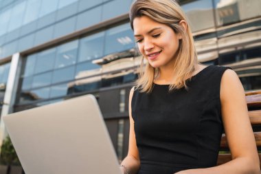 Sokakta otururken dizüstü bilgisayarını kullanan genç iş kadınının portresi. İş konsepti.