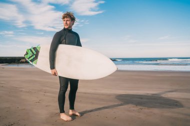 Genç sörfçü siyah sörf takımıyla okyanusta duruyor. Spor ve su sporları konsepti.