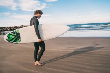 Genç sörfçü siyah sörf takımıyla okyanusta duruyor. Spor ve su sporları konsepti.