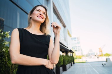 Ofis binalarının önünde duran genç iş kadınının portresi. İş ve başarı kavramı.