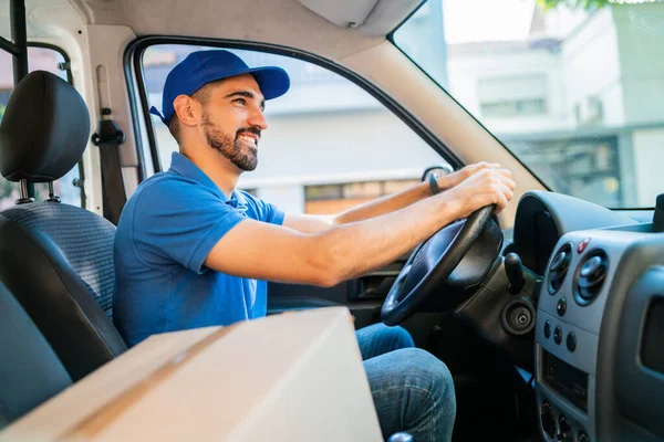 Portrait of a delivery man driver driving van with cardboard boxes on seat. Delivery service and shipping concept.