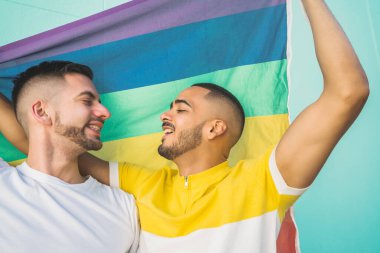 Sokakta gökkuşağı bayrağıyla sarılıp sevgilerini gösteren genç eşcinsel çiftin portresi. LGBT ve aşk konsepti