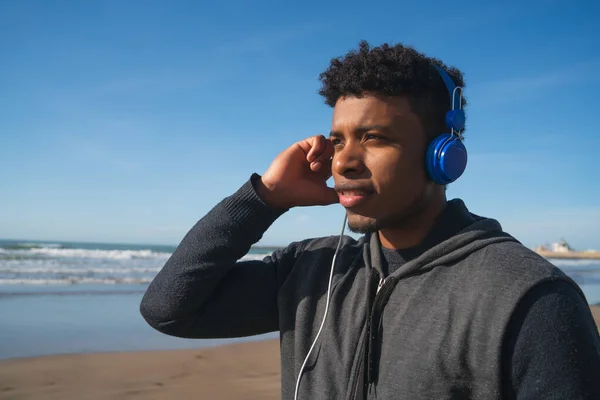 Portrait of an athletic man listening to music with earphones while resting for exercise at the beach. Sport and healthy lifestyle.