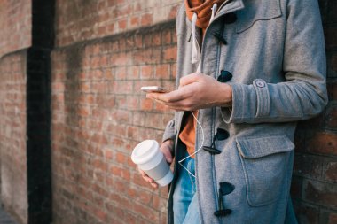 Kulaklıklı genç bir adamın portresi ve tuğla duvara karşı cep telefonu kullanması. Açık havada. Şehir konsepti.